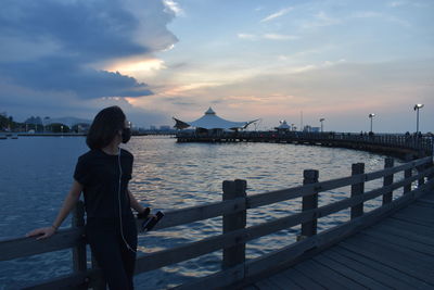 Girl standing on pier over sea against sky during sunset