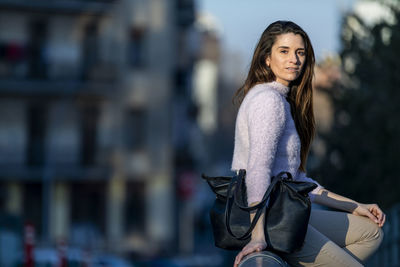 Portrait of woman sitting on railing in city