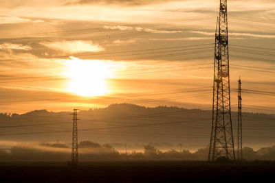 Silhouette electricity pylon on field against sky during sunset