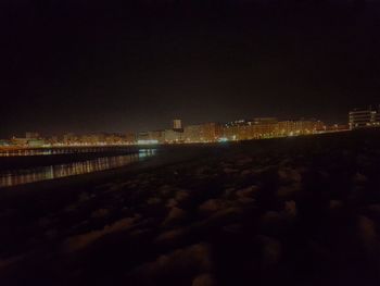 Illuminated buildings by river against sky at night