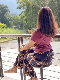 Rear view of woman sitting on railing against trees