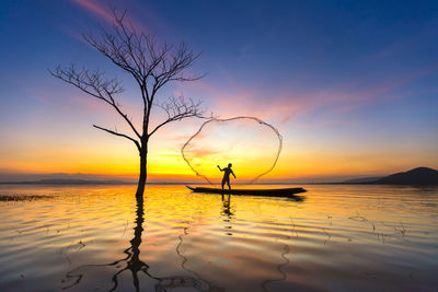 Silhouette man by bare tree against sky during sunset