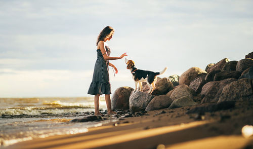 Side view of woman standing on rock by sea against sky