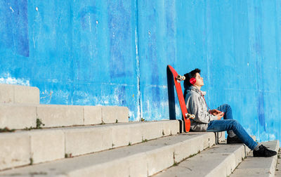 Teenager with headphones listening music while sitting on staircase.