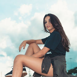 Portrait of young woman sitting against sky