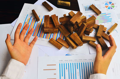 Cropped hand of man gesturing by wooden blocks on graph and charts
