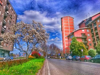 Road leading towards buildings against cloudy sky