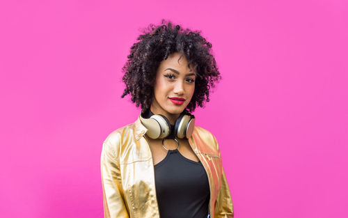 Fashionable young woman with curly hair against pink background