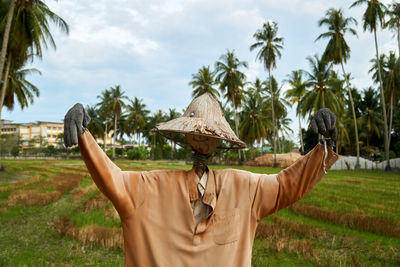 Man standing by palm trees on field against sky