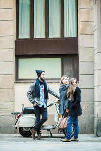 Full length of friends standing against building on sidewalk