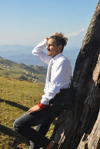 A young guy moving his hand on hair with leaning against tree