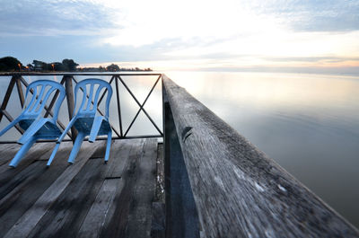 Blue chairs on pier in lake against sky