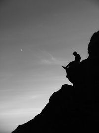 Low angle view of person sitting on rock formation against sky