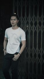 Portrait of young man standing against metal fence