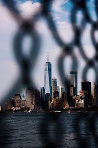 Modern buildings by river in city seen through fence