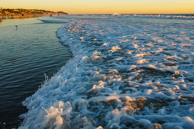 Ocean wave with foam on surface and sunset lights 