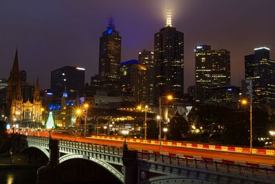 Illuminated bridge and buildings against sky at night