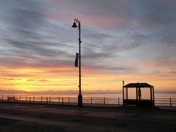 Silhouette street by sea against sky during sunset