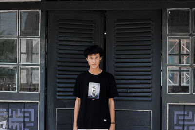 Portrait of young man standing against window