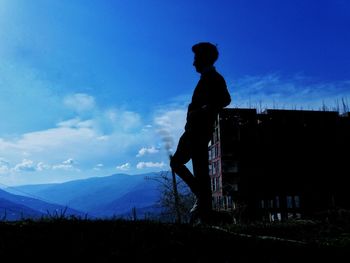 Silhouette man standing on mountain against blue sky