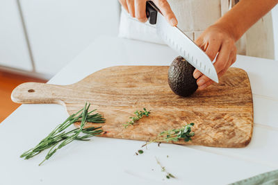 Hands cutting hass avocado on cutting board with rosemary and thyme