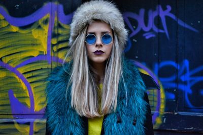 Close-up portrait of young woman standing by graffiti wall