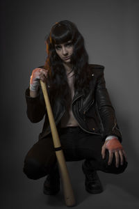 Portrait of young female model crouching with baseball bat against gray background