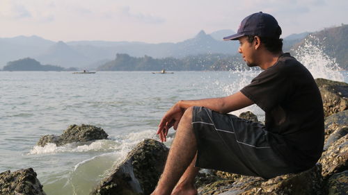 Side view of young man sitting on rock by sea