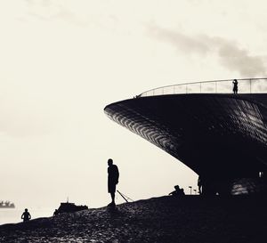 Silhouette people walking on beach against sky