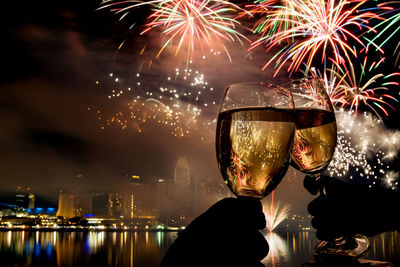 Close-up of wine glasses toasting against fireworks at night