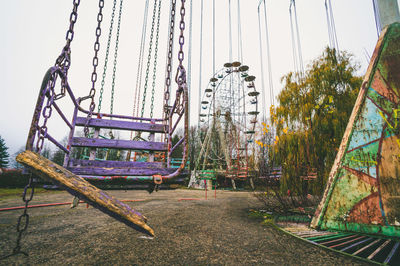 Abandoned carousel swings in closed amusement park and broken ferris wheel