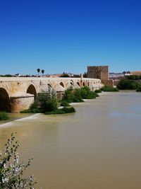 Arch bridge over river against clear blue sky