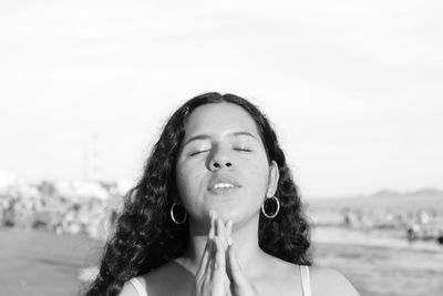 Beautiful young woman with eyes closed praying against sky