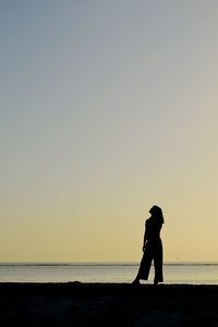 Silhouette woman standing on beach against clear sky