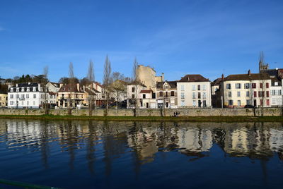 Buildings by lake against blue sky