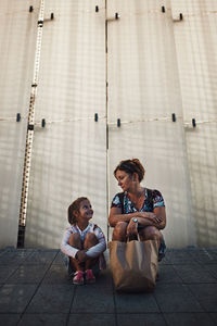 Mother and her little daughter resting in a public place outdoors after shopping in the evening