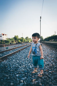 Cute boy standing on railroad track against clear sky