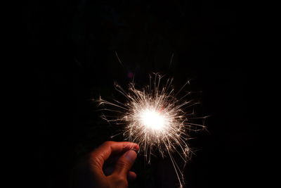 Cropped hand holding sparkler at night