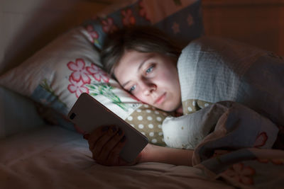 High angle view of cute boy using mobile phone while lying on bed at home