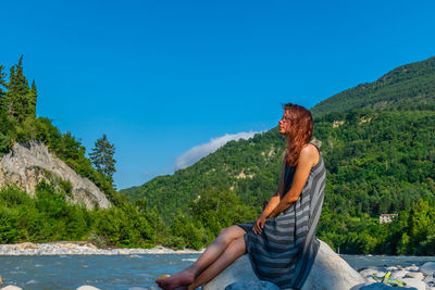 Full length of woman siting on rock by river in forest