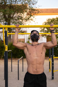 Shirtless man wearing mask exercising at park