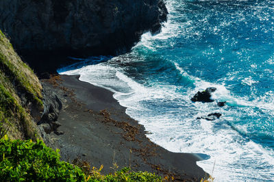 High angle view of sea waves lapping hidden cove of black sand surrounded by cliffs.