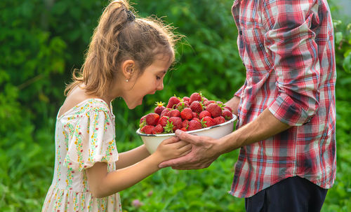 Hands of man showing bowl of strawberries to surprised girl