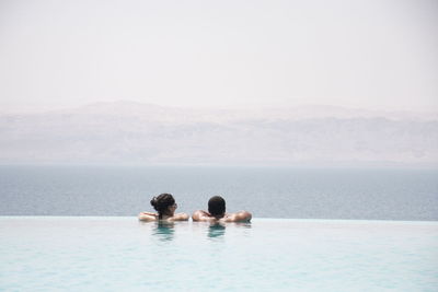 Rear view of couple in infinity pool against sea