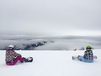 Rear view of people snowboarding on snow covered mountain against cloudscape