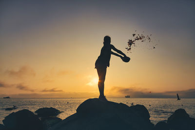 Silhouette man standing on rock at beach against sky during sunset