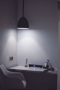 Illuminated lamp on table against wall at home