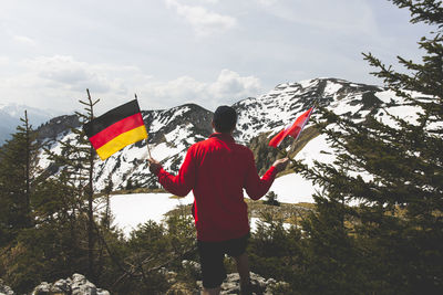 Rear view of mature man holding national flags while standing against snowcapped mountain