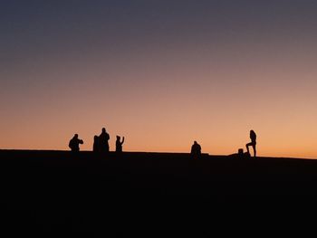 Silhouette people walking on beach against sky during sunset