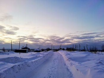 Snow covered road against sky during sunset